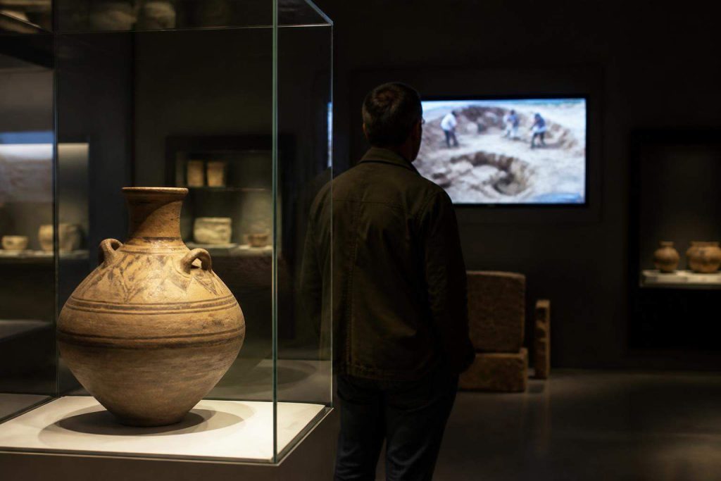 Visitante observa una pieza arqueológica y un vídeo documental en una sala de museo.
